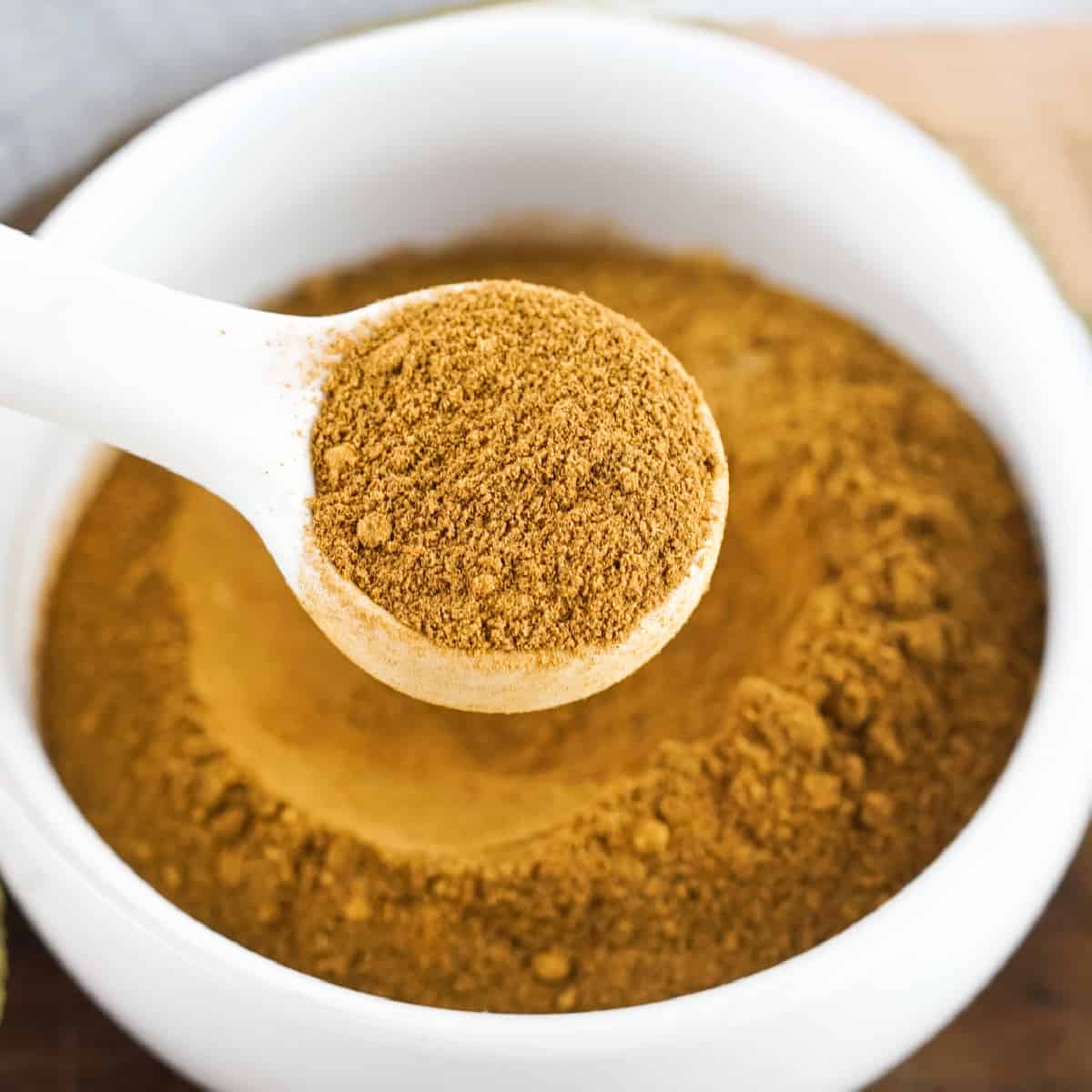 Pumpkin spice mix in a white bowl with a white round spoon lifting some of it. 