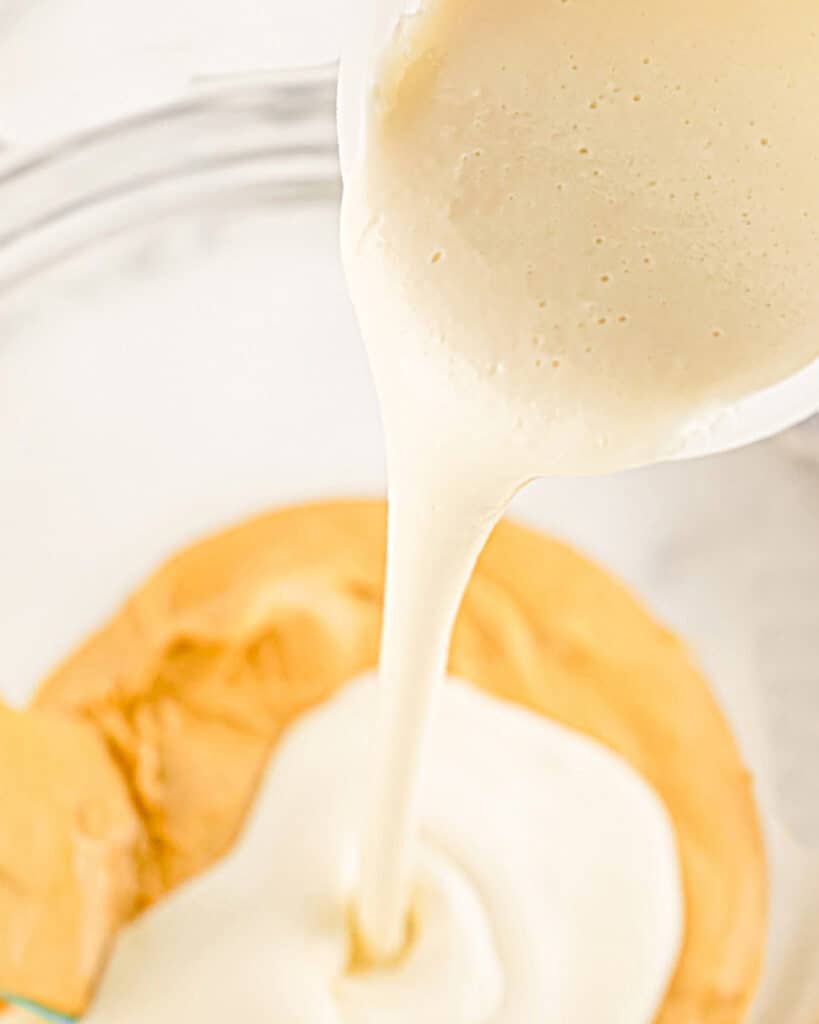 Pouring melted white frosting onto melted peanut butter chips in a glass bowl.