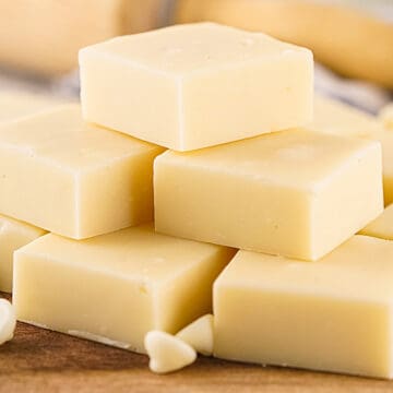 Pile of white chocolate fudge squares on a wooden surface.