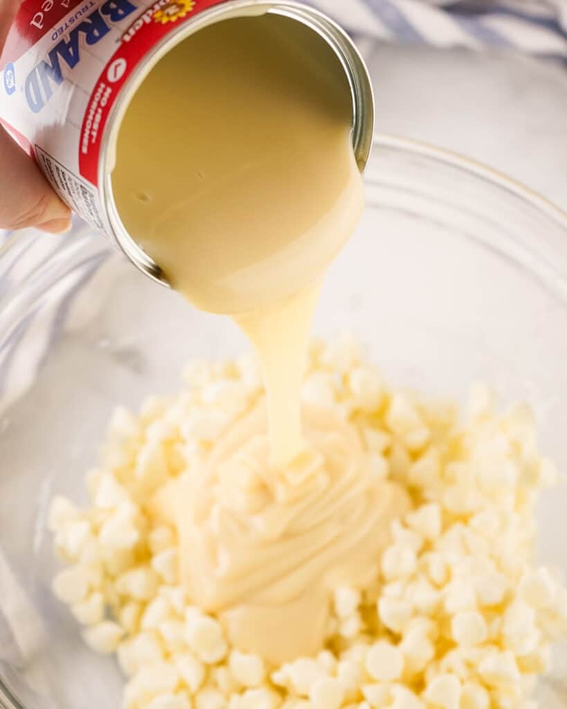Pouring condensed milk into glass bowl with vanilla chocolate chips.