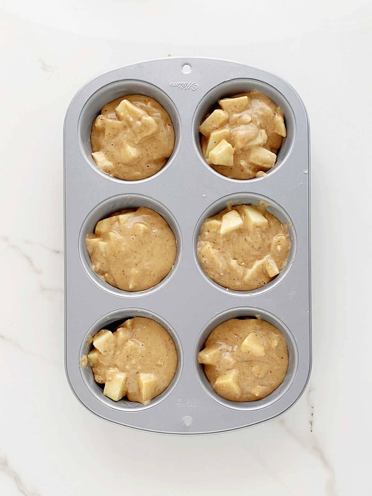 Apple muffins batter in jumbo metal pan on a white marbled surface. Top view.