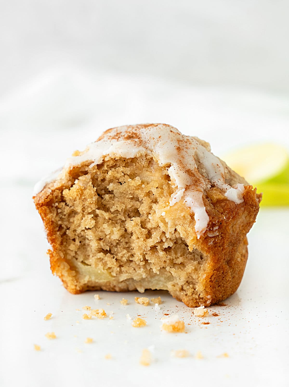 Half eaten apple crumb muffin with glaze on a white background.