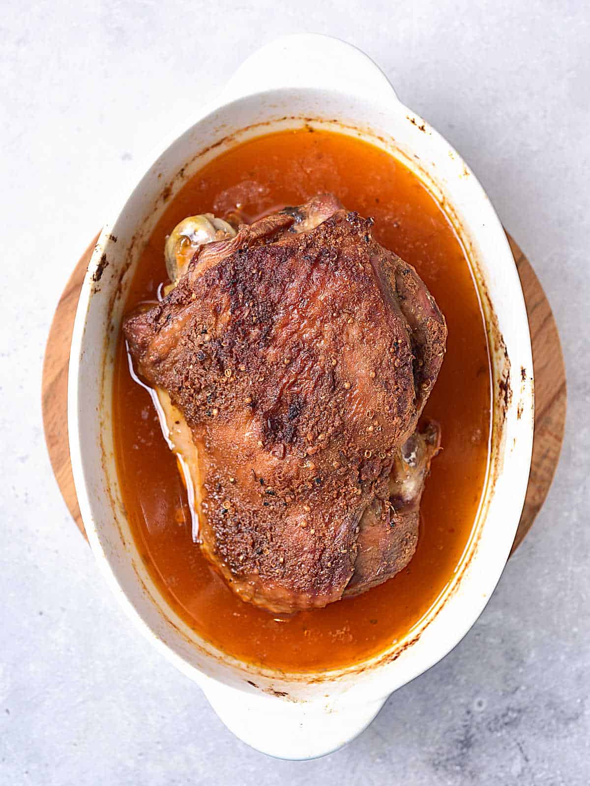 Baked seasoned turkey thigh in an oval white dish on a light grey surface.