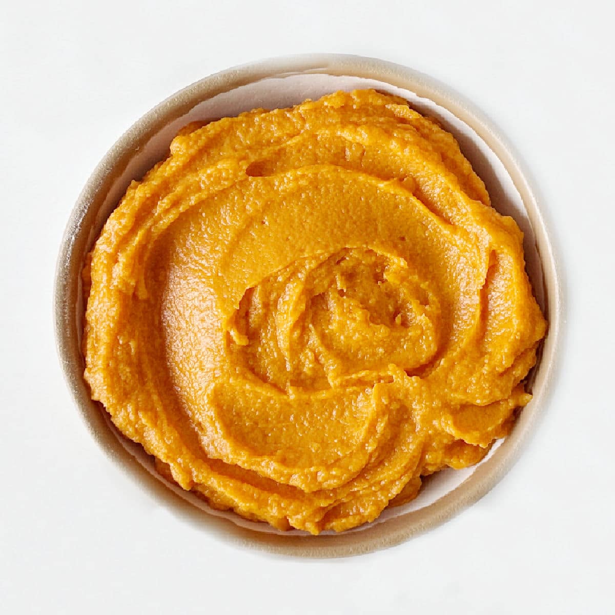 Top view of bowl with sweet potato puree on a white surface.