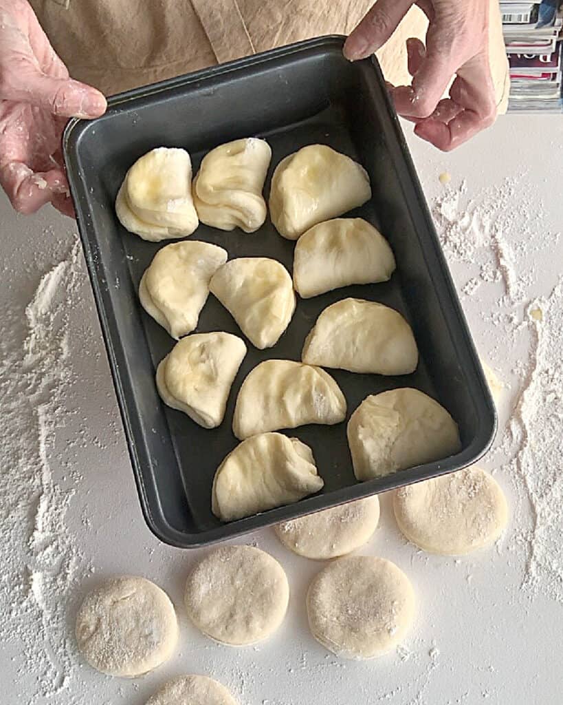 Rectangular dark metal pan with Parker house buns before last rise.