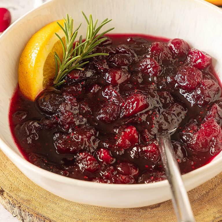 Close up of cranberry orange sauce in a white bowl with a spoon. Wooden board surface.