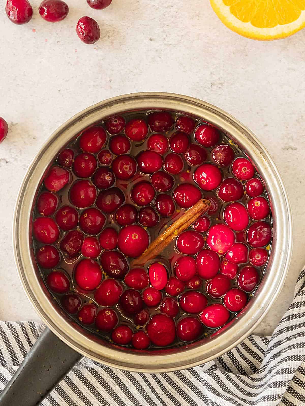 Metal saucepan with cranberries before cooking. Beige surface, striped cloth.