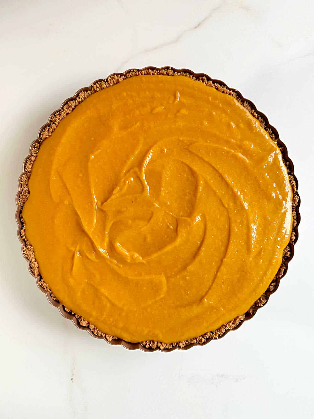 Round metal pan with sweet potato pie filling on a white surface. Top view.