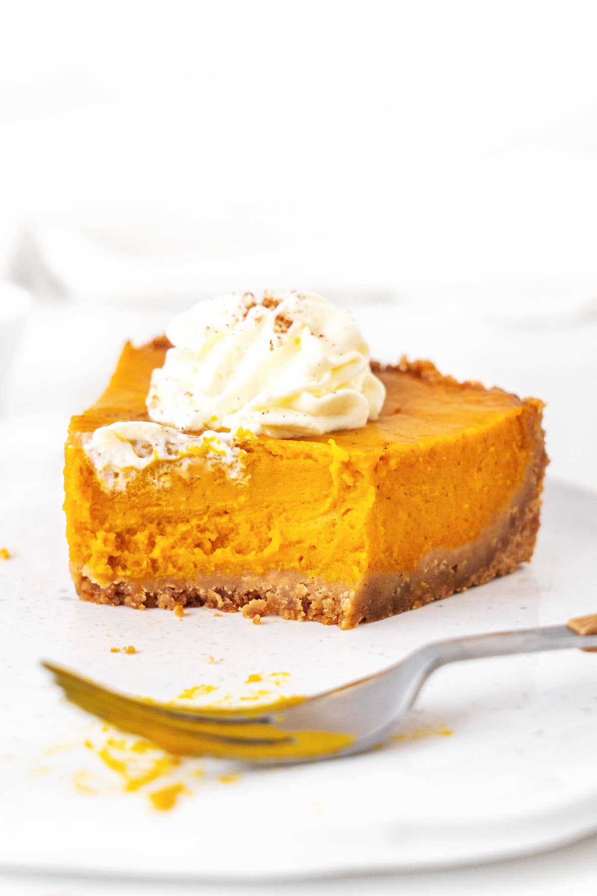 Half eaten sweet potato pie slice with cream on a white plate. Silver fork. White background.