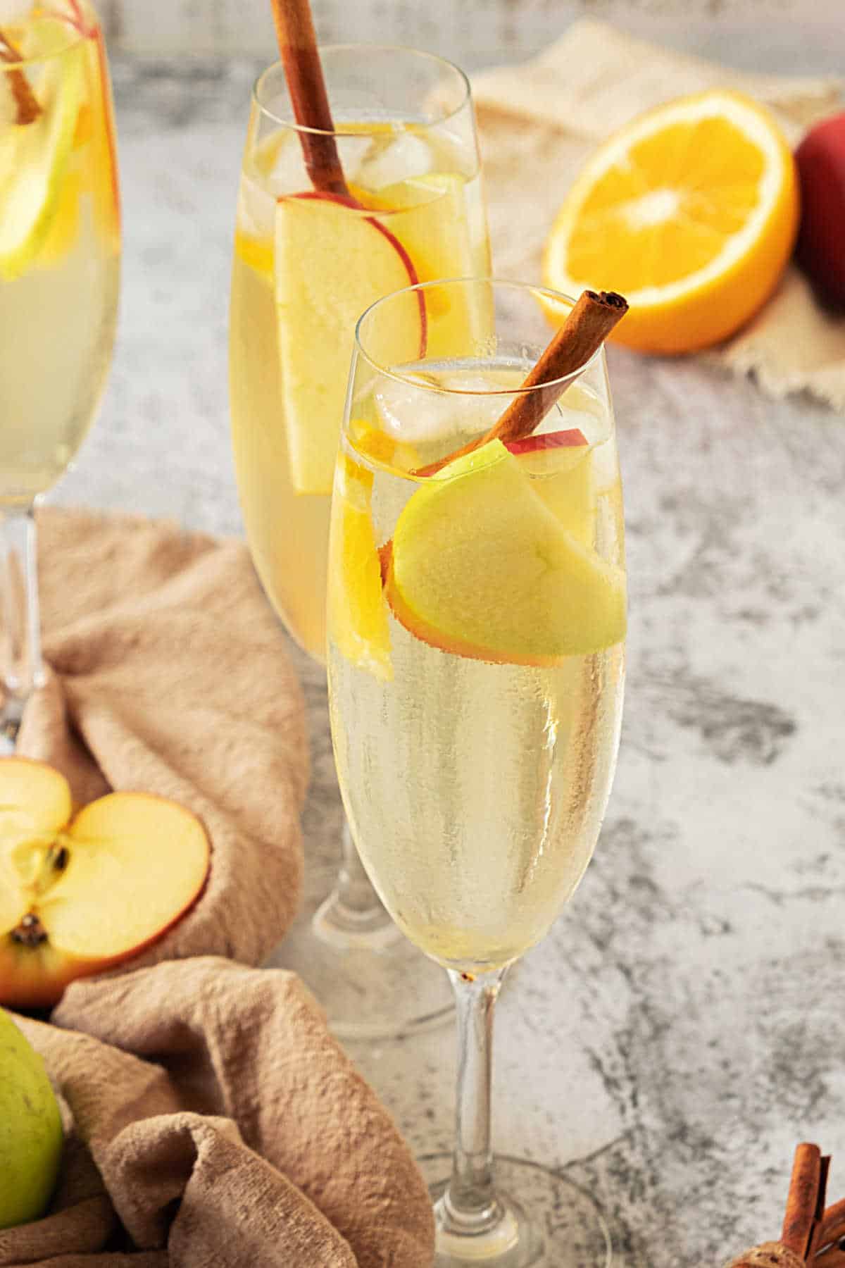 White wine apple cider sangria in long stemmed glasses with apple slices and cinnamon. Grey background. Brown cloth.