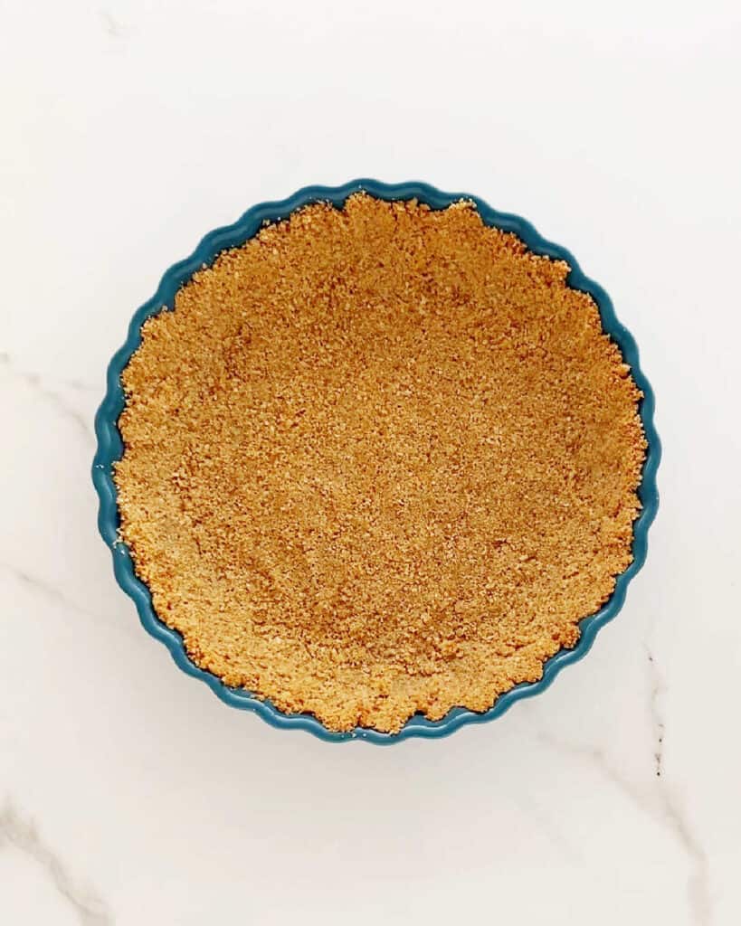 Teal pie dish with graham cracker crust on a white marbled surface.
