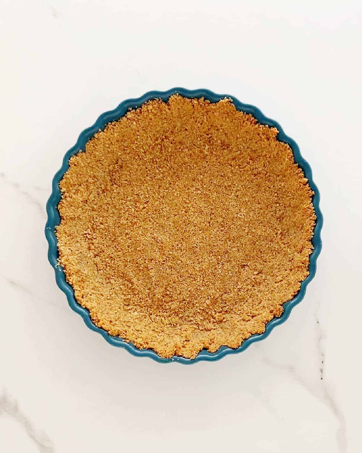 Teal pie dish with graham cracker crust on a white marbled surface.
