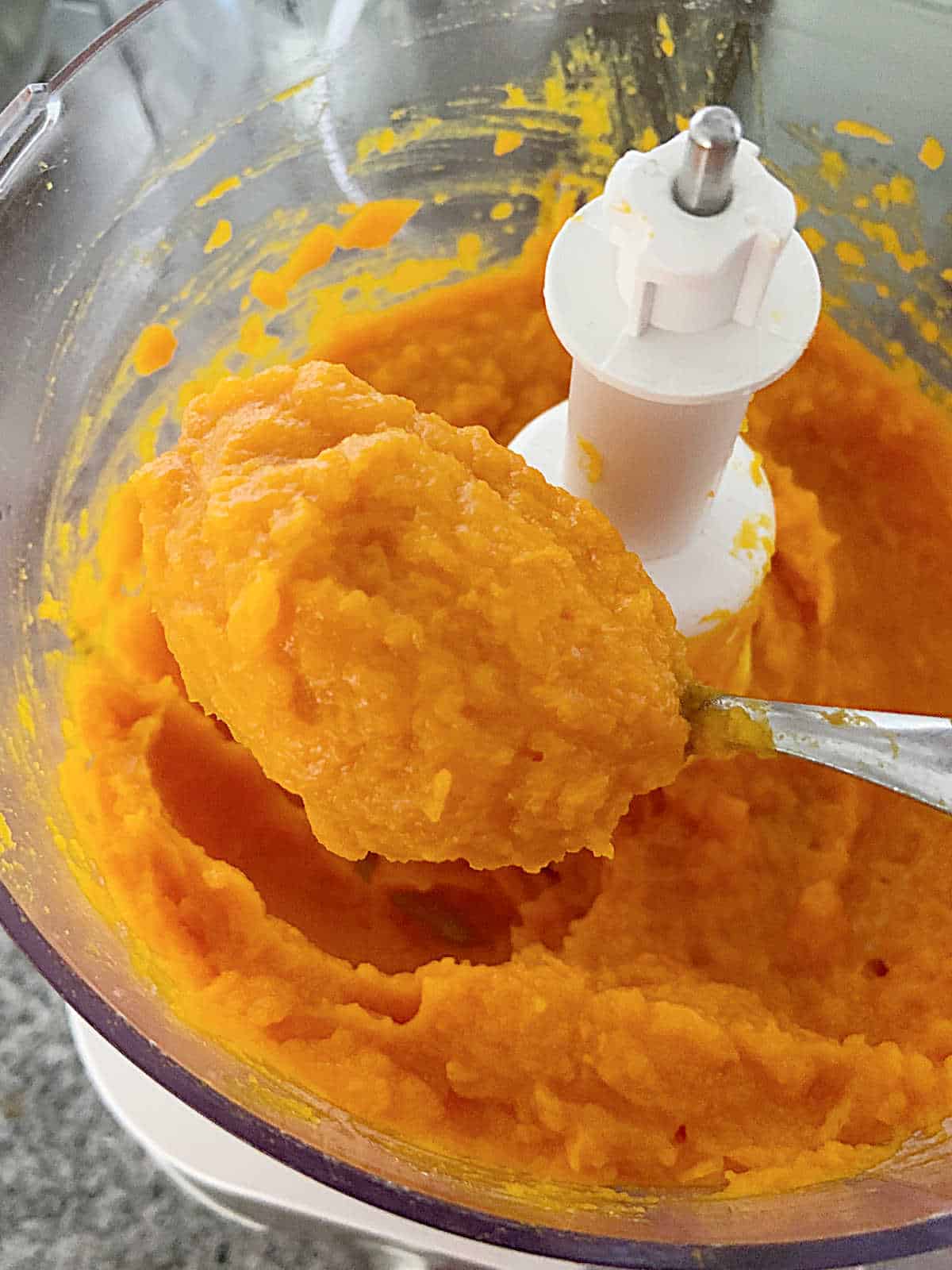 Spooning sweet potato puree from a food processor jar.