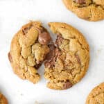 Close up of halved warm milk chocolate chip cookie on white parchment paper.