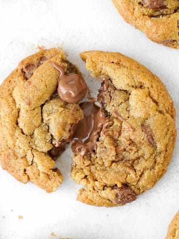 Close up of halved warm milk chocolate chip cookie on white parchment paper.