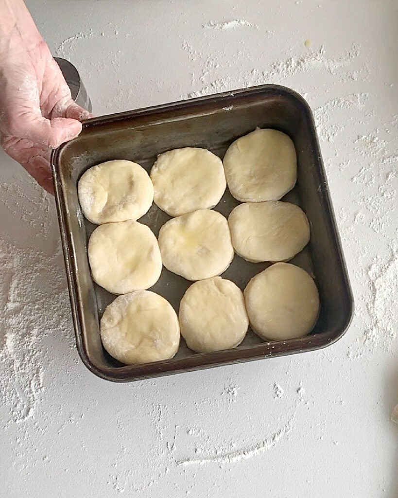 Dark metal pan with buns before last rise. White background.