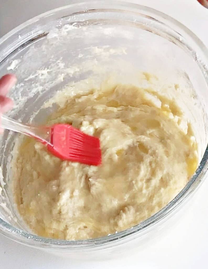 Glass bowl with parker house rolls batter. Red brush with butter.