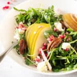 Close up of white bowl with pear, arugula and pomegranate salad.