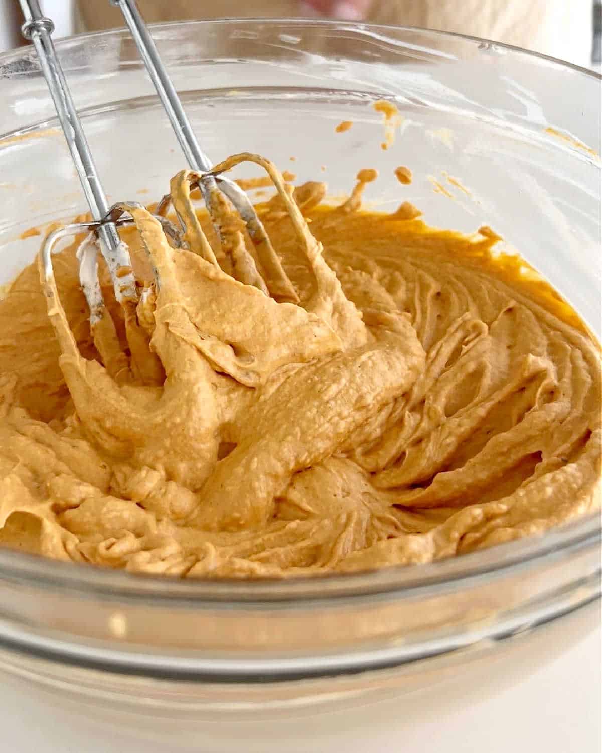 Pumpkin mixture for pie in a glass bowl with electric beaters.