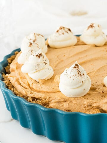 Pumpkin mousse pie with whipped cream rosettes on a teal dish. White background.