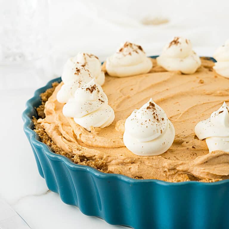 Pumpkin mousse pie with whipped cream rosettes on a teal dish. White background.