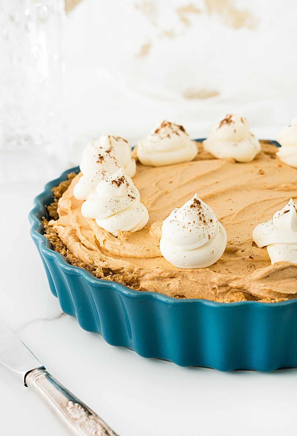 Partial front view of teal ceramic dish with pumpkin mousse pie with cream rosettes. White background. 