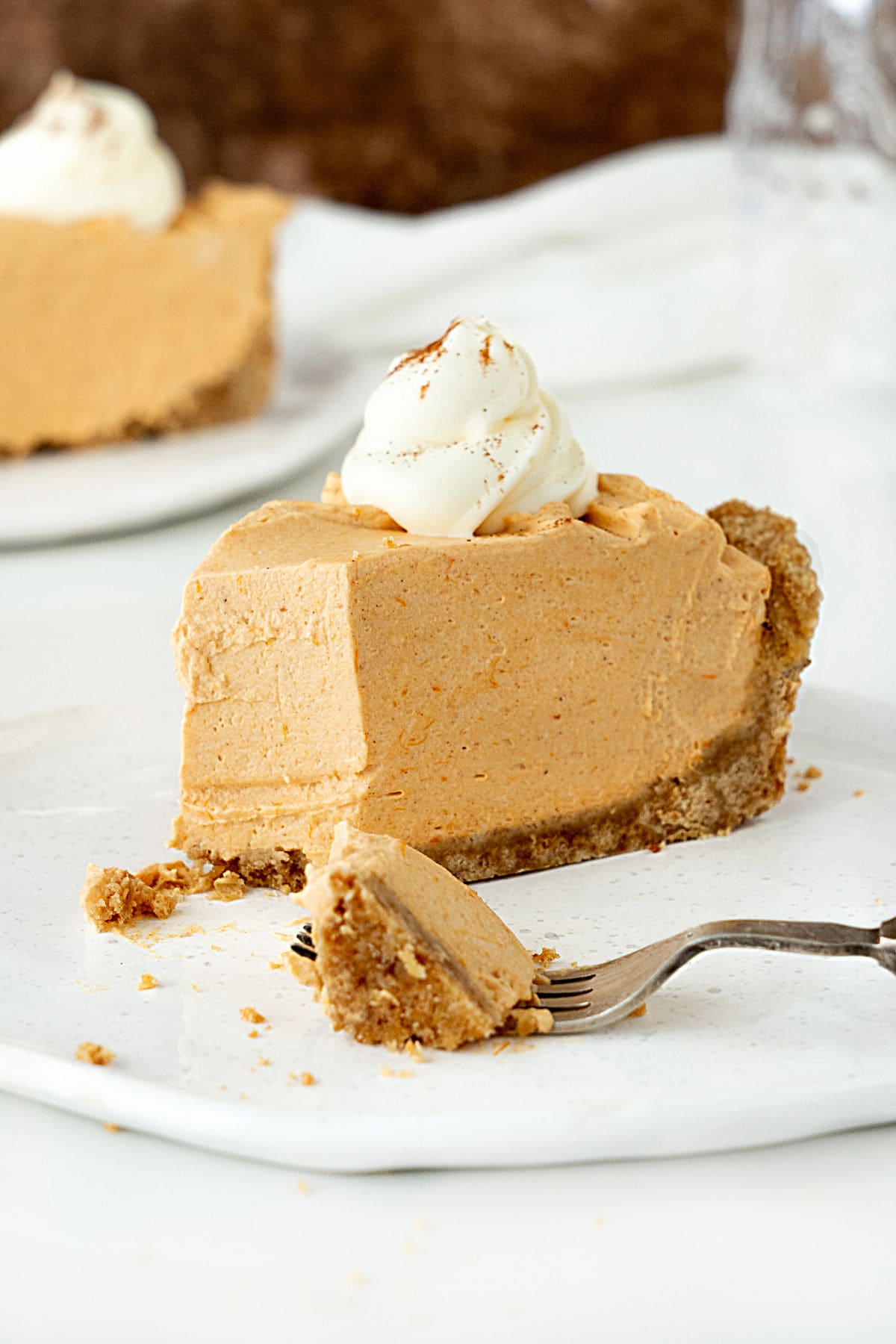 White plate with slice of pumpkin mousse pie, a piece in a fork. White and brown background.