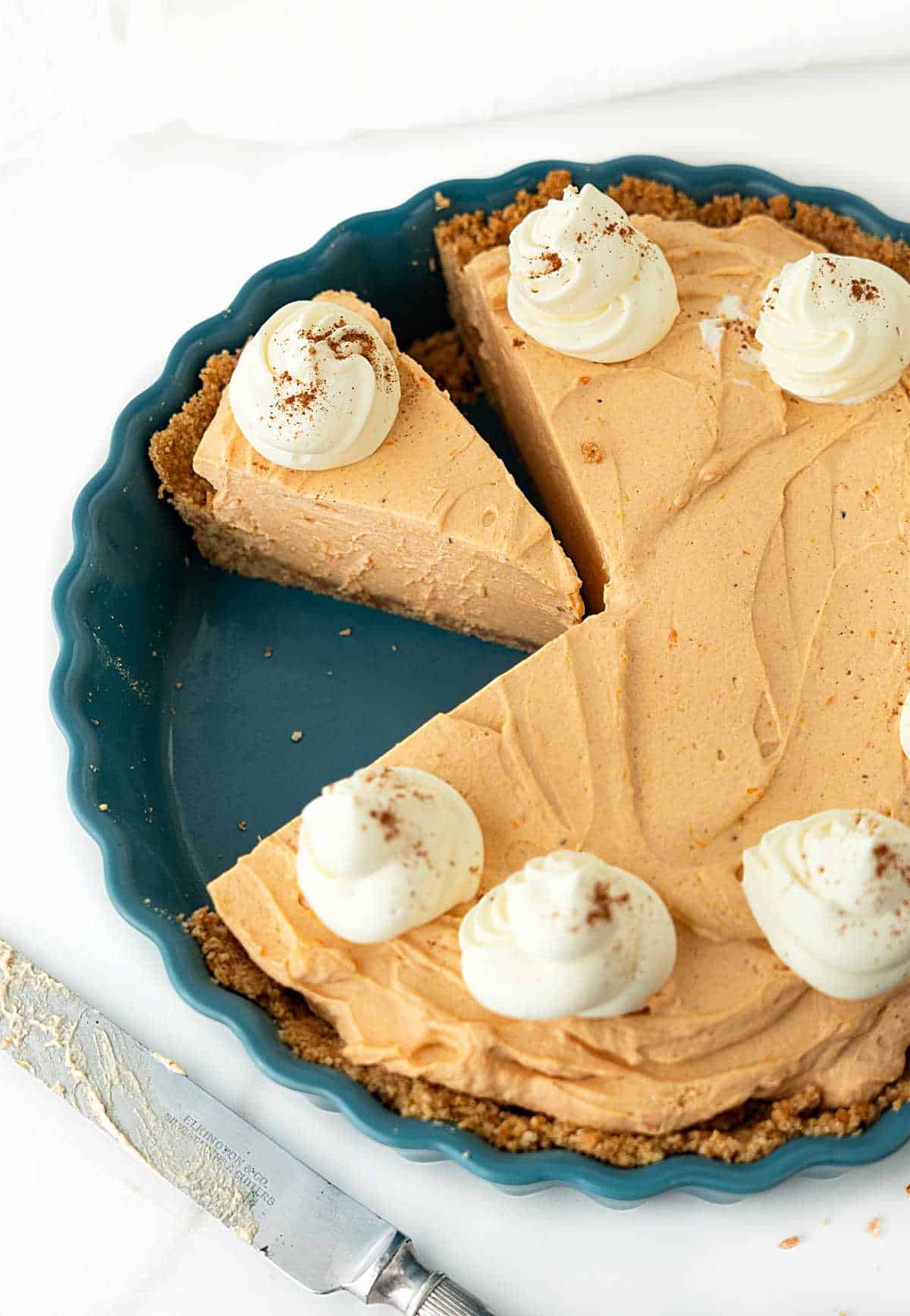 Top view of pumpkin mousse pie in a teal dish, some are cut. White background.