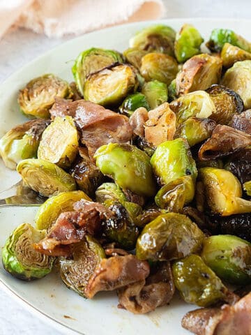 White bowl with roasted brussels sprouts with bacon. White surface, pink cloth.