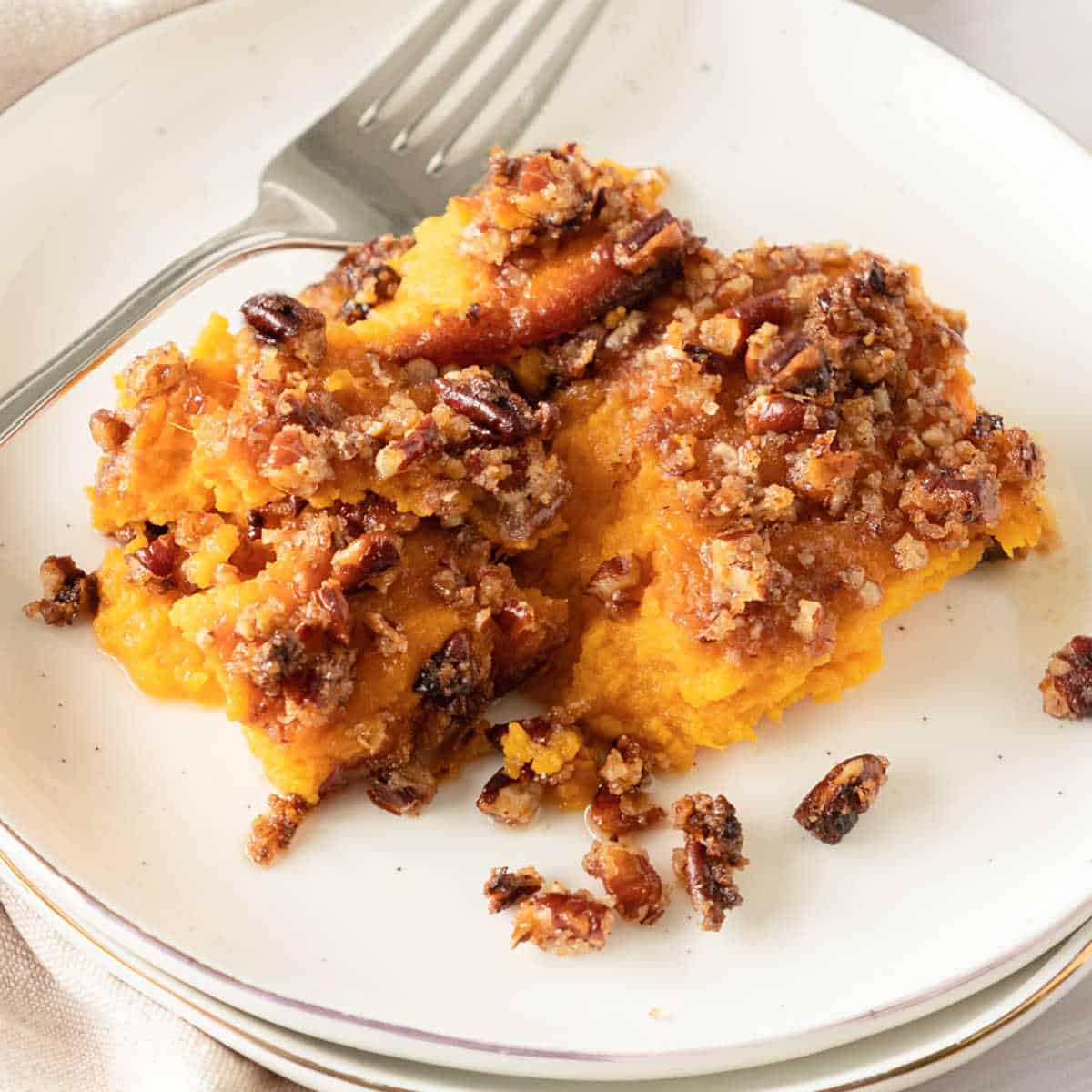 White plate with serving of sweet potato casserole with pecan topping. A silver fork.