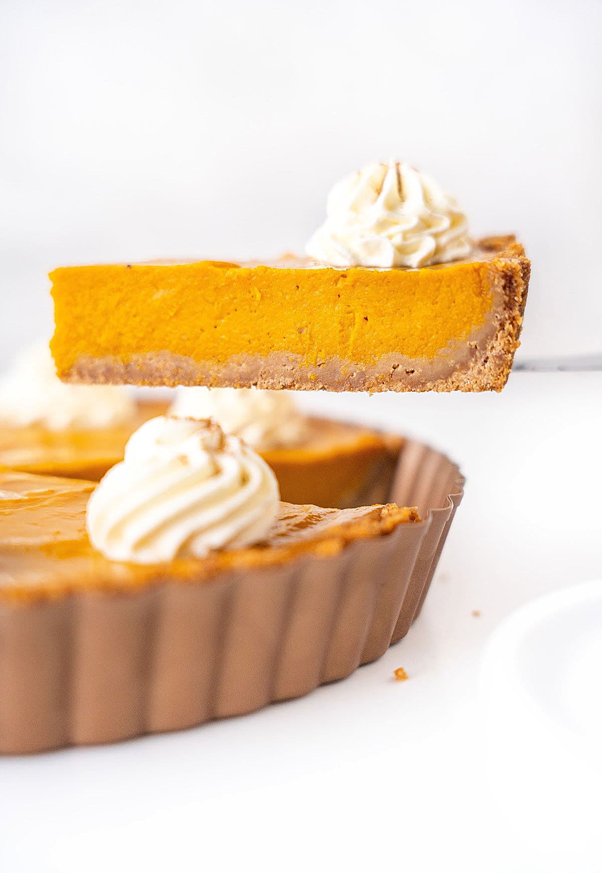 Lifting a slice of sweet potato pie with cream from a metal pan. White surface and background. 