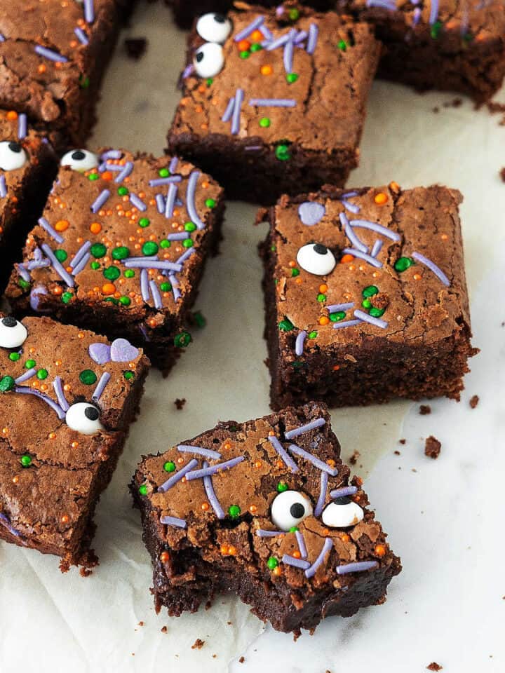 Brownie squares with Halloween sprinkles and candy eyes on a white surface.