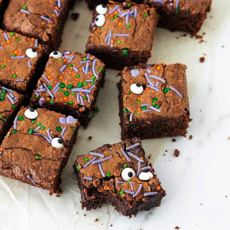 Brownie squares with Halloween sprinkles and candy eyes on a white surface.