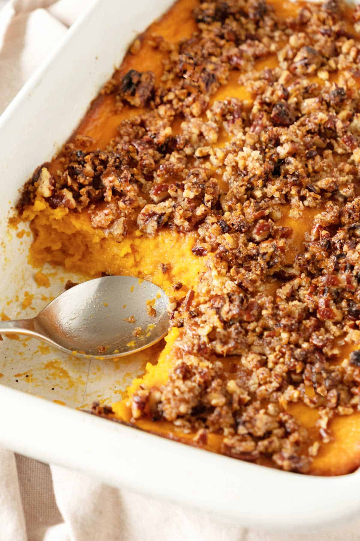 Serving missing in a pecan sweet potato casserole. Silver spoon, white rectangular dish. 