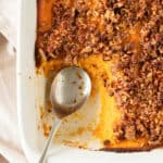 Close up of half eaten sweet potato pecan casserole on a white dish. Silver spoon inside.