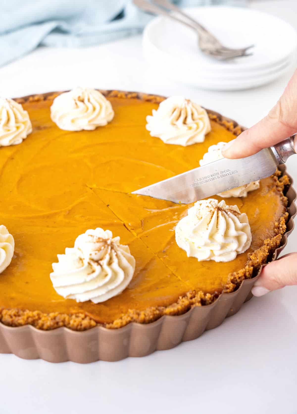 Cutting sweet potato pie with whipped cream in a metal pan. White background.