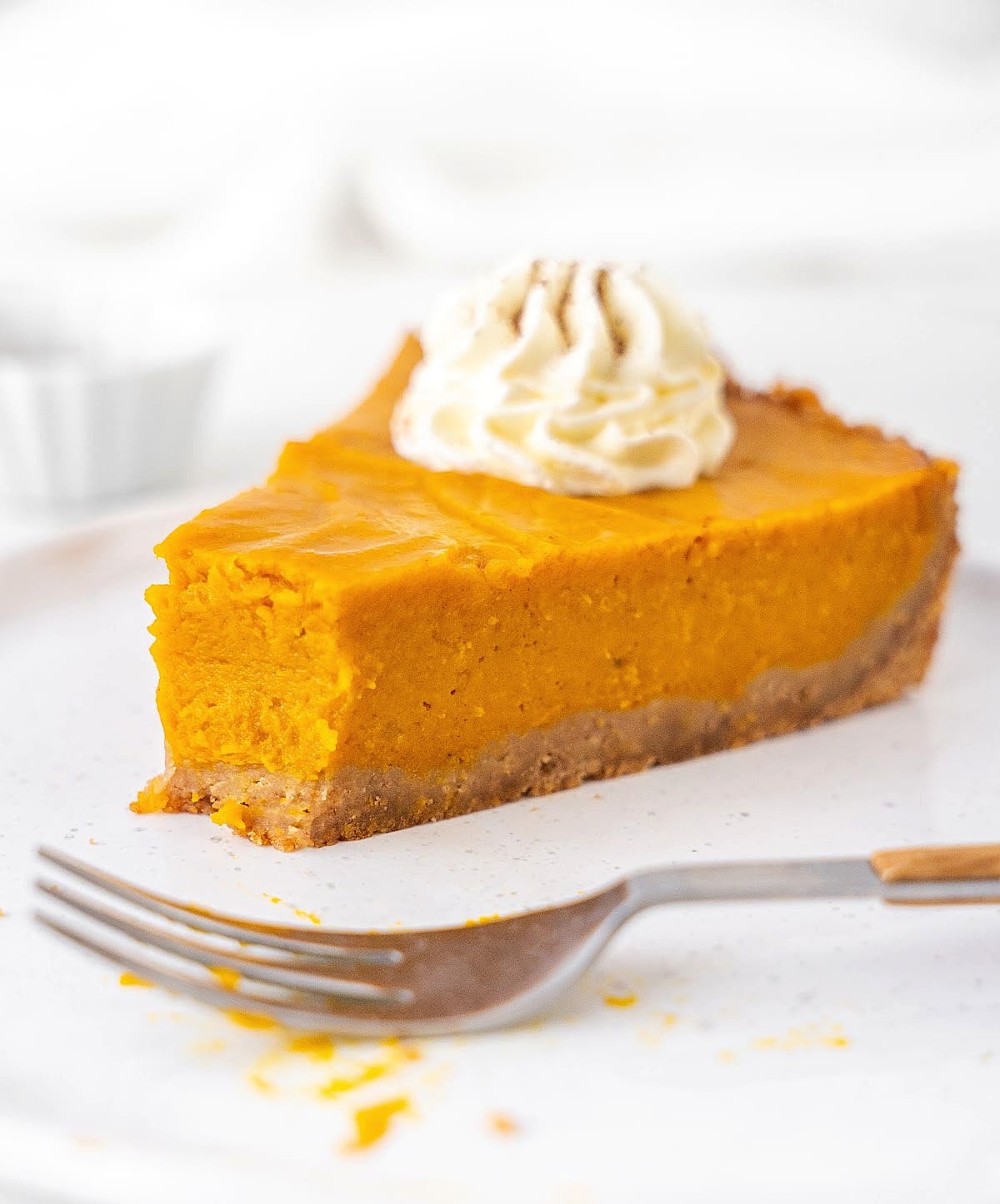 Bitten slice of sweet potato pie with graham crust and cream on a white plate. Silver fork. White background. 