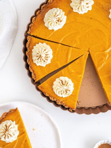 Cut sweet potato pie with cream in the pan on a white surface. Slice on a white plate.