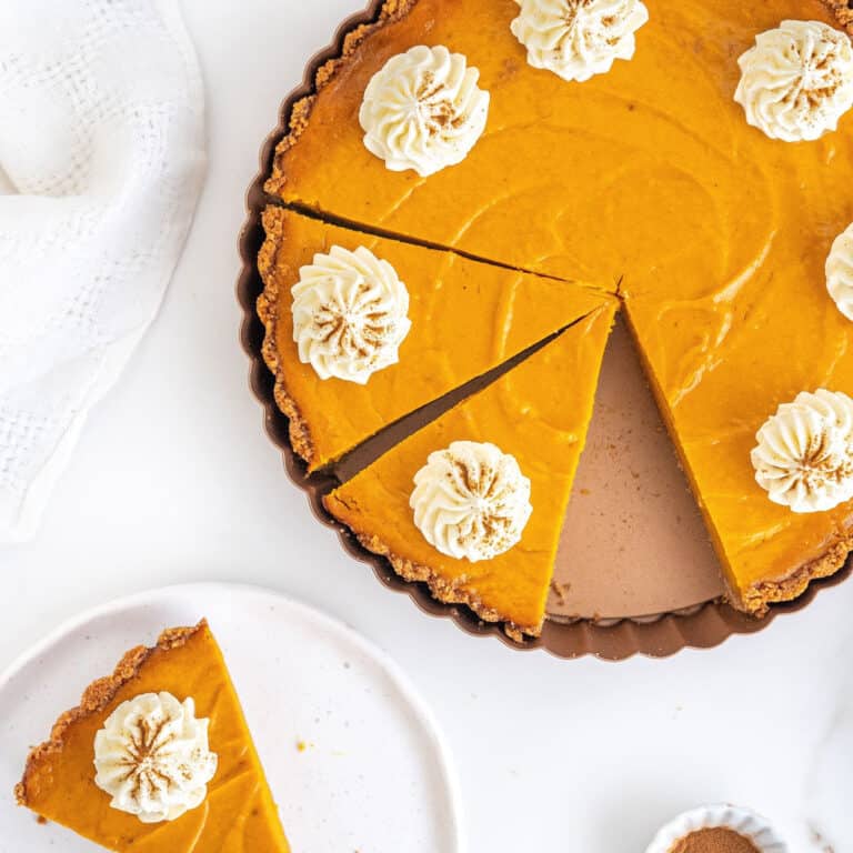 Cut sweet potato pie with cream in the pan on a white surface. Slice on a white plate.