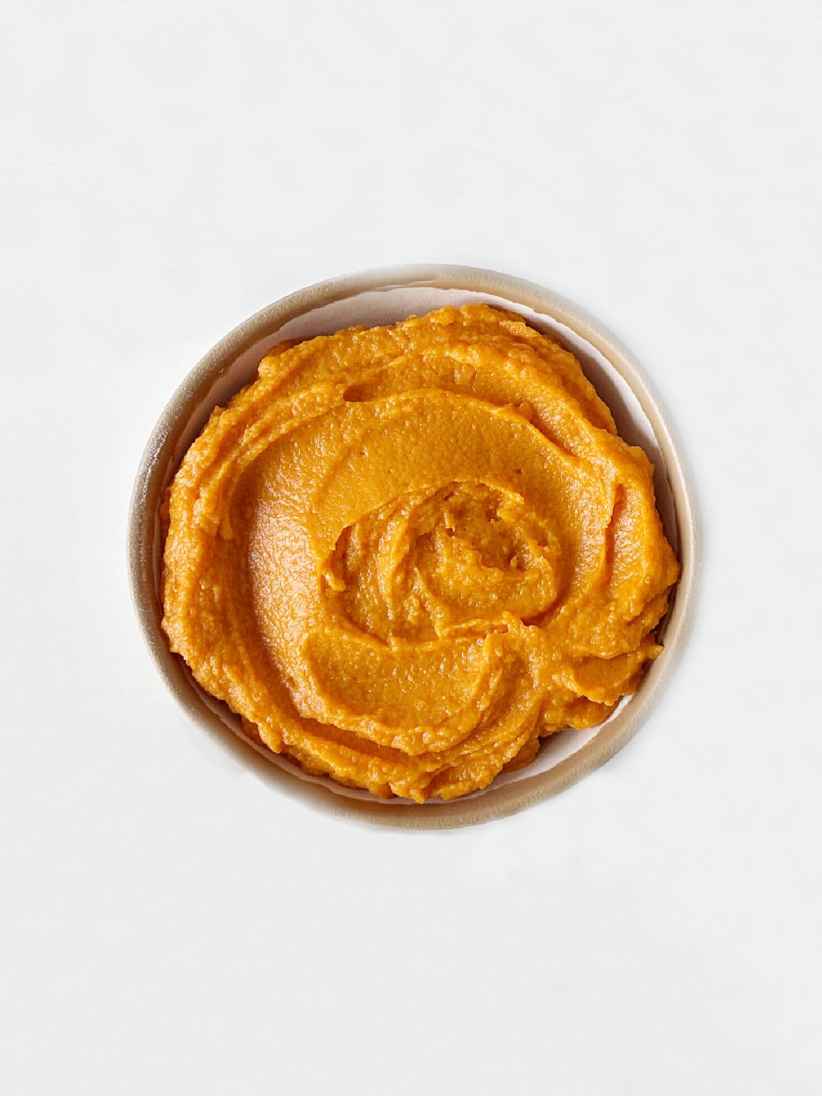 A bowl with sweet potato puree on a white surface. Top view. 