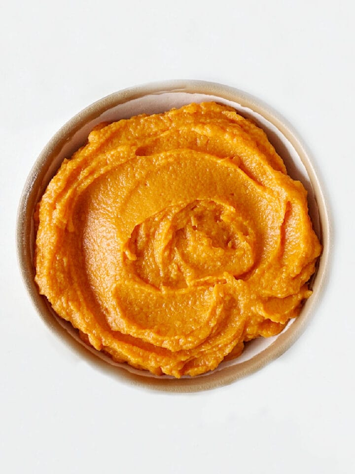 Top view of bowl with sweet potato puree on a white surface.