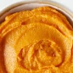 Close up sweet potato puree in a bowl with white background. Orange text overlay.