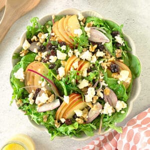 Top view of shallow bowl with apple walnut green salad with feta and cranberries. White surface.