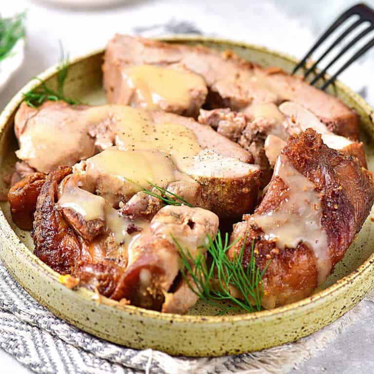 Close up of sliced turkey thighs with homemade gravy on a green plate. White and grey surface.