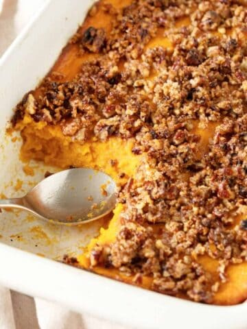 Serving missing in a pecan sweet potato casserole. Silver spoon, white rectangular dish.