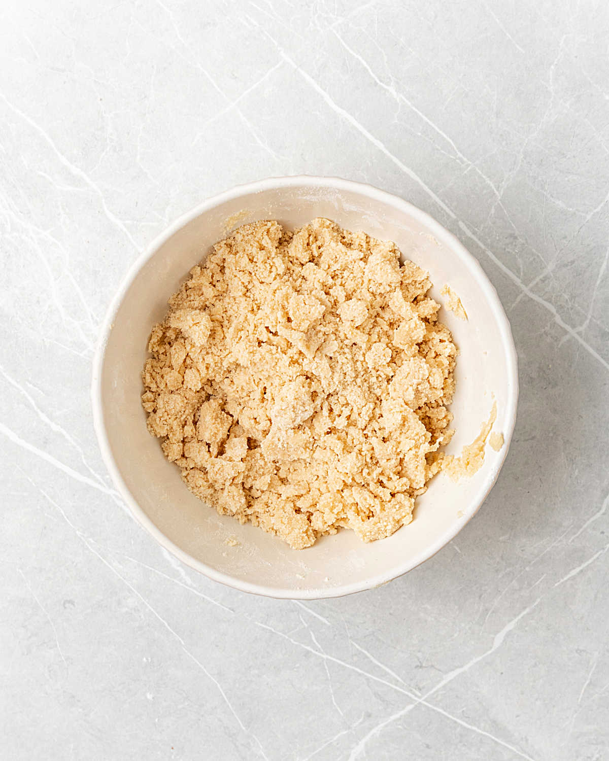 Crumb topping with brown sugar in a white bowl on a light grey surface. 