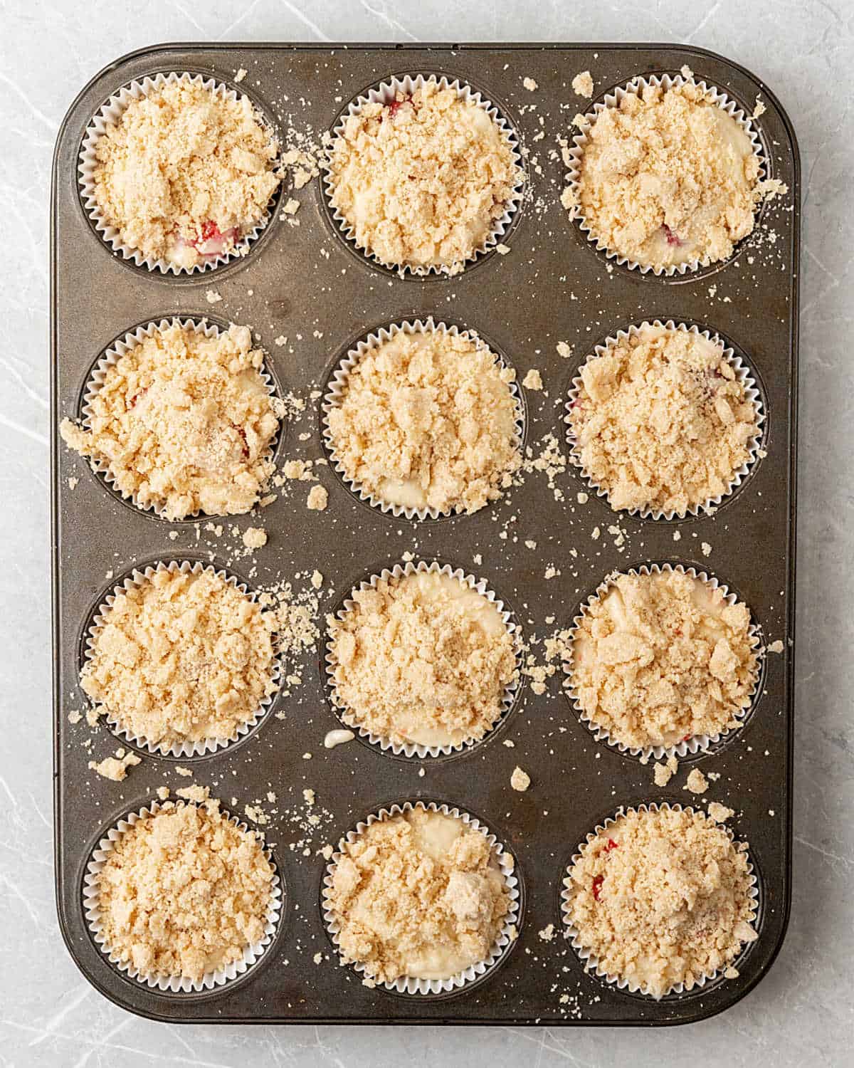 Crumb muffins in a muffin pan before baking. Light grey surface.