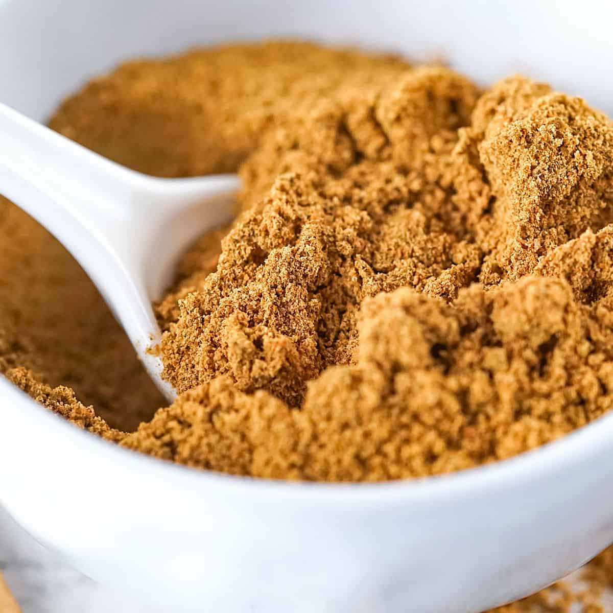 Close up of homemade gingerbread spice in a white bowl with a white spoon.