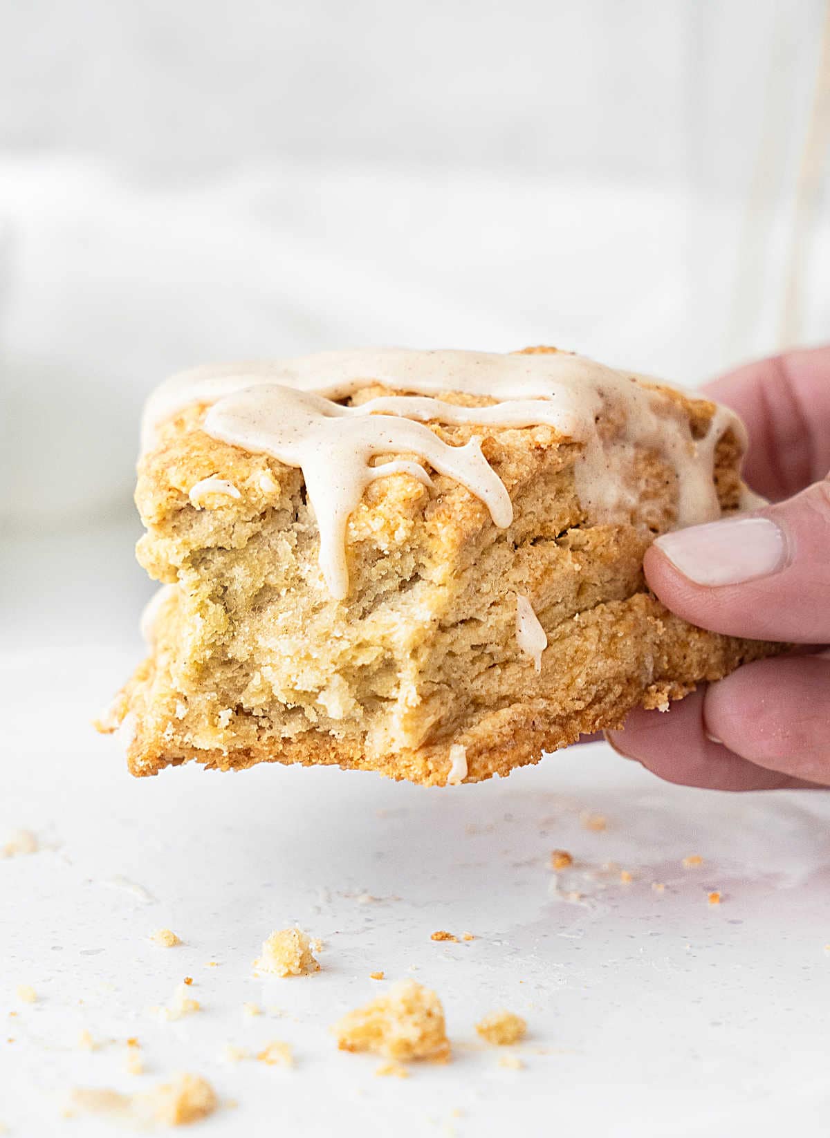 Holding a bitten cinnamon scone with glaze on a white background. 