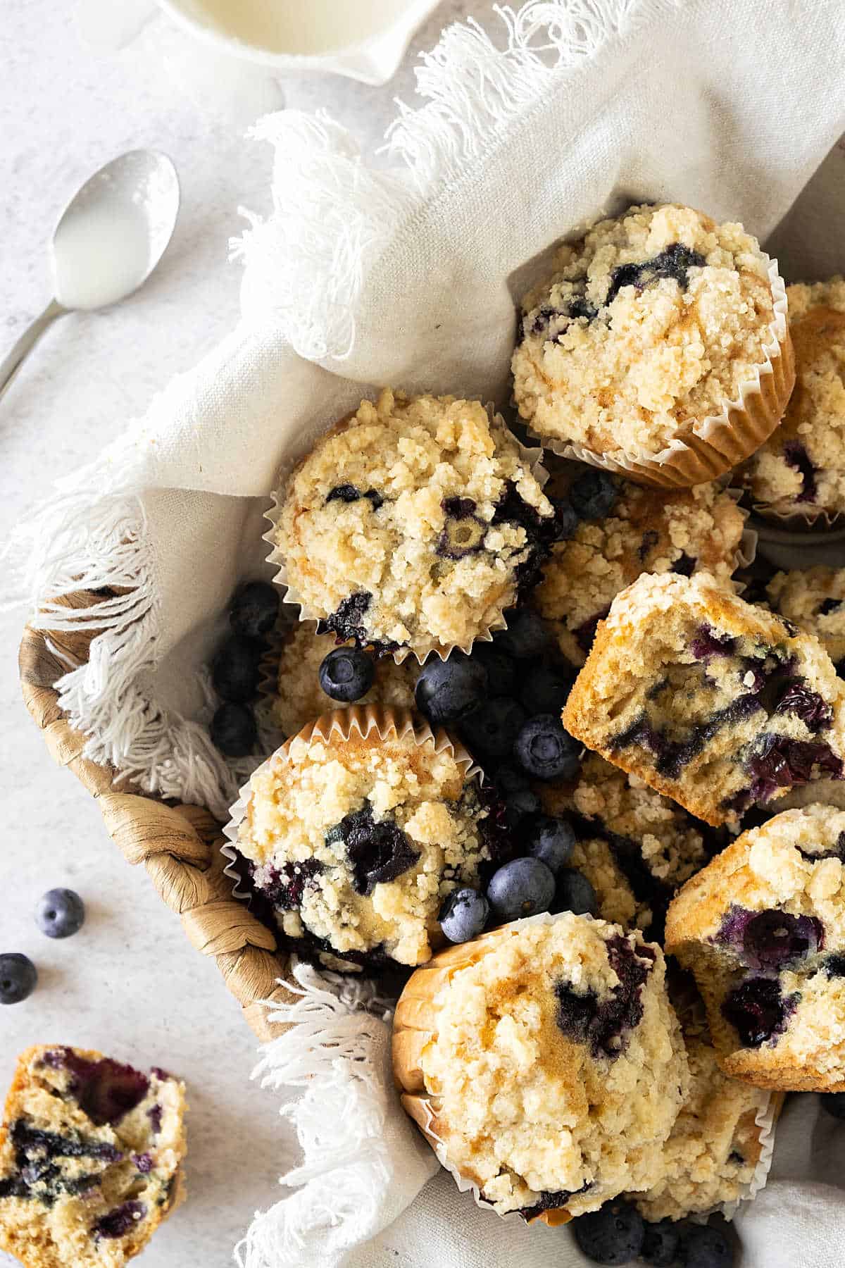 White towel in a basket with pile of blueberry crumb muffin.